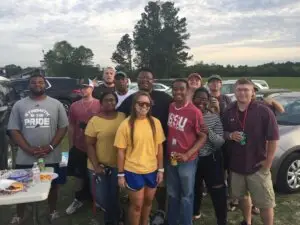 College students gather in front of cars to pose for a picture