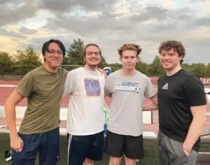 4 guys pose for a picture with arms around each other on soccer field