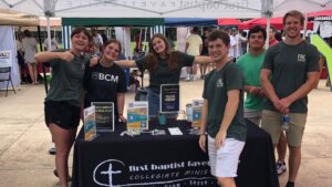 Members of First Baptist Fayette stand under tent in front of table on college campus