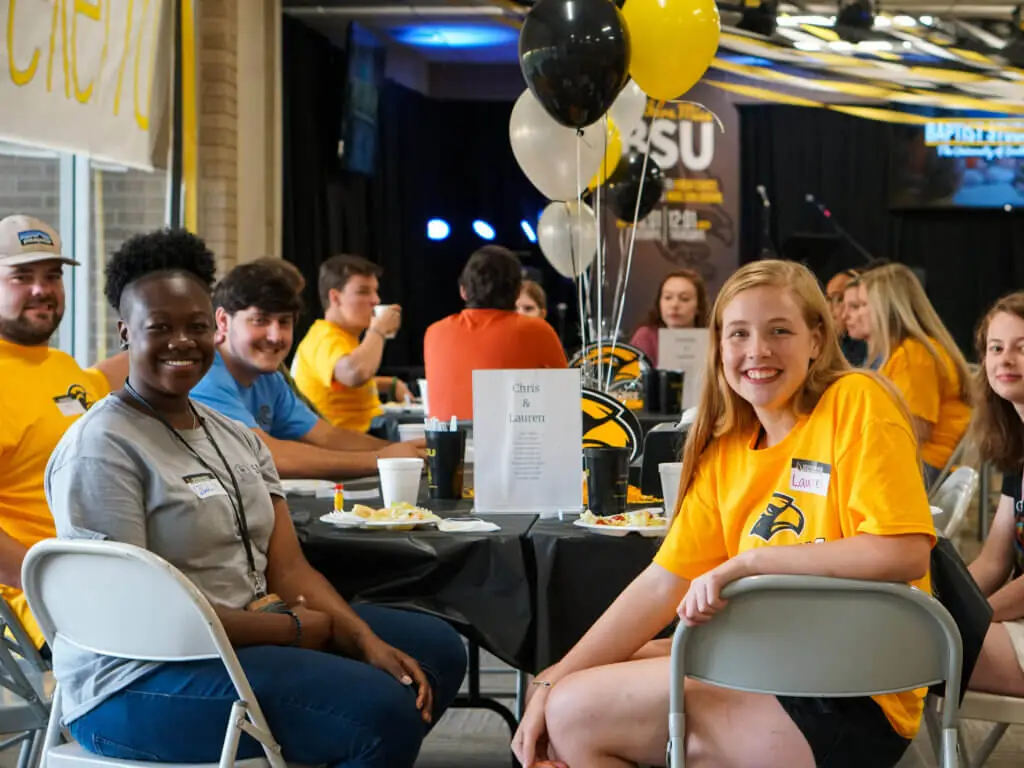 Students sitting around table with gold and black balloons on it pose for a picture