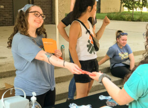 Girl hands student free item and information about campus ministry