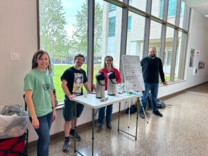 A small group of people stand behind table offering free chai to students on a college campus