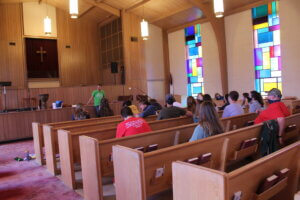 College students sitting in wooden pews in small church with stained glass windows