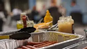 Hotdogs sitting in aluminum pan with condiments in the background