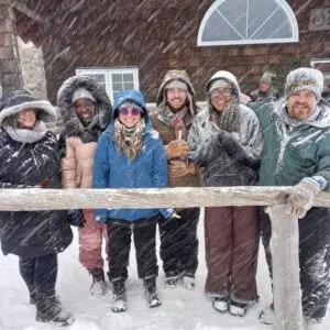 Group of college students stand together for a photo in the snow with flurries coming down