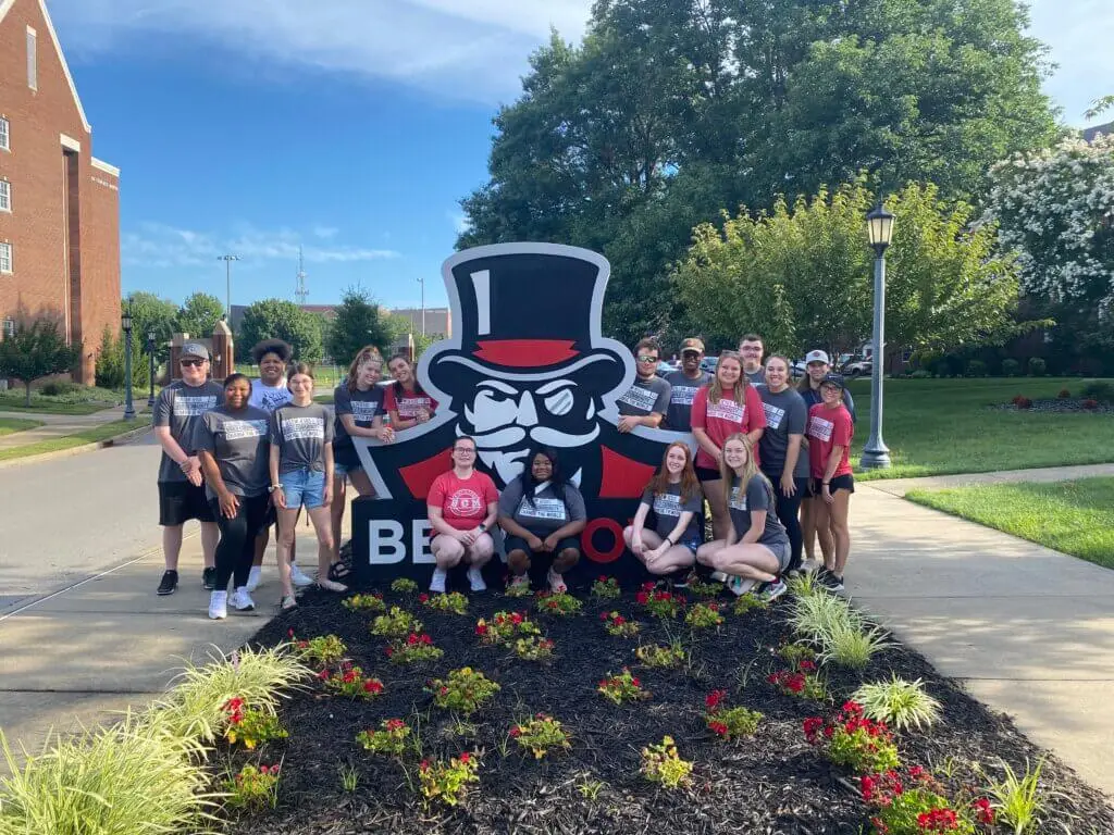 College students pose standing around sign on campus