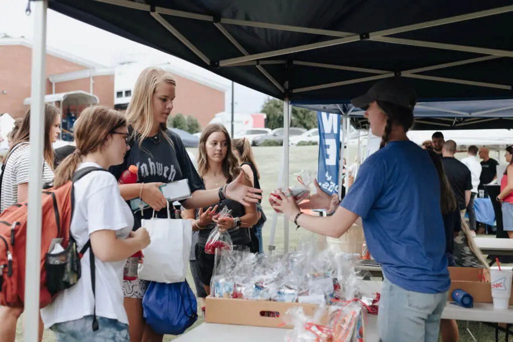 Woman standing under a tent hands out gift bags to college students on campus