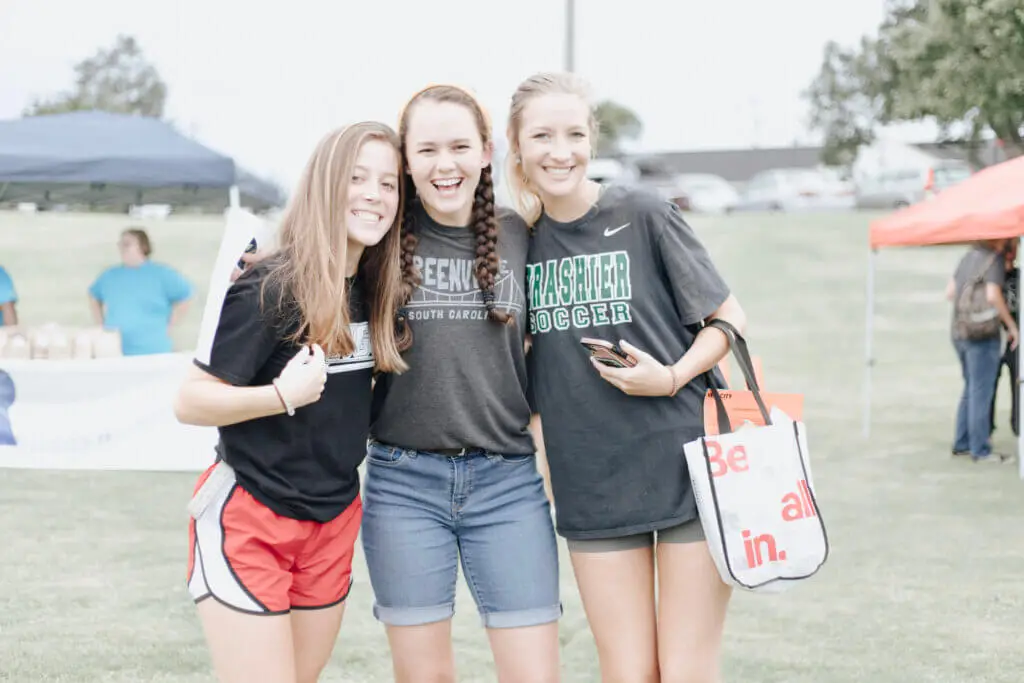 Three female students pose together at a church fair on their college campus