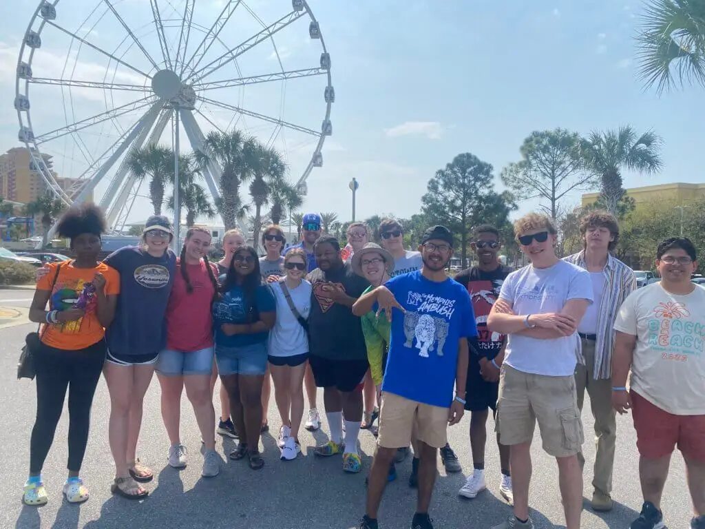 College students pose in front of ferris wheel in parking lot