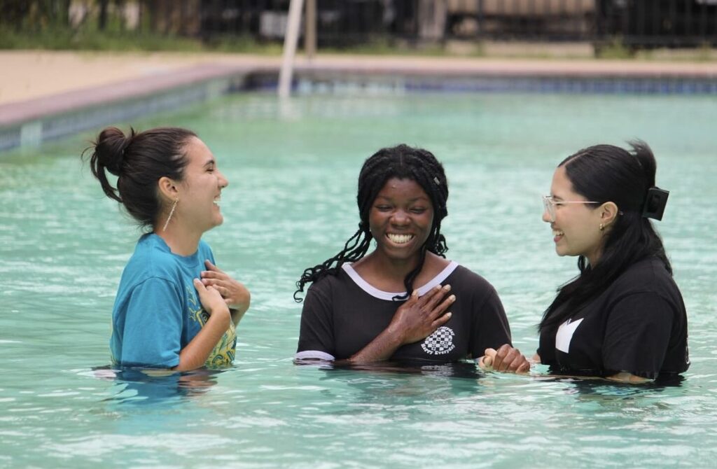 Three girls stand in a pool for baptism