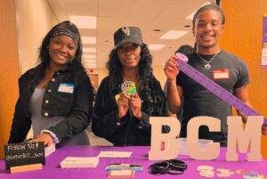 Three college students stand behind table with purple BCM table cloth