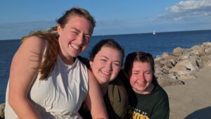 Three college girls smiling at the beach in front of the ocean.