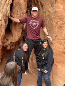 Two college students lift up a college student in between red canyon rocks.