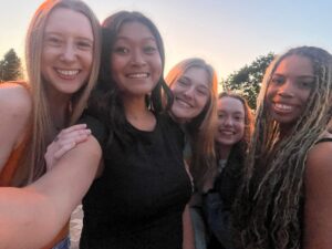 A group of college girls pose for a selfie outside at sunset.