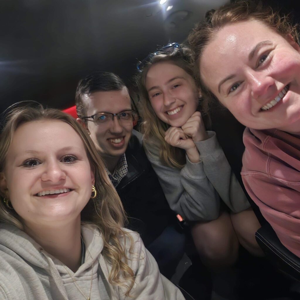 Four college students pose for a picture in a car at night.