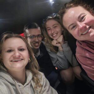 Four college students pose for a picture in a car at night.